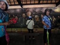 This picture taken on June 13, 2019 shows visitors taking photos in front of a mural, illustrating the efforts to rescue of the 12 boys from the "Wild Boars" football team and their coach after they were trapped in the Tham Luang cave last year, at the cave's visitor centre in the Mae Sai district of Chiang Rai province. Lillian SUWANRUMPHA / AFP