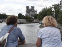 People stand on the river bank as they look towards the Notre-Dame de Paris cathedral on June 15, 2019. Zakaria ABDELKAFI / AFP