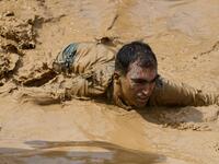 A runner crawls in mud as he takes part in the Mud Day, a 13km race with obstacles in Beynes, near Paris on June 16, 2019.  ALAIN JOCARD / AFP
