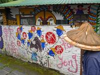 This picture taken on March 30, 2019 shows a local resident walking past a house painted by Hakka graffiti artist Wu Tsun-hsien in the Taiwanese village of Ruan Chiao. Nestled in the mist-covered foothills of Taiwan's central mountain range, Ruan Chiao village is virtually devoid of young people, but artist Wu Tsun-hsien is coaxing the Instagram generation back by transforming local homes into a canvas of colour. Sam YEH / AFP