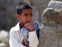 A Yemeni boy holds his notebooks as school children attend an open-air class under a tree near their unfinished school  Ahmad AL-BASHA / AFP