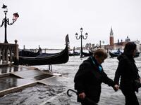 People walk across the Ponte della Paglia bridge, past a stranded gondola after an exceptional overnight "Alta Acqua" high tide water level, early on November 13, 2019 in Venice. Powerful rainstorms hit Italy on November 12, with the worst affected areas in the south and Venice, where there was widespread flooding. Within a cyclone that threatens the country, exceptional high water were rising in Venice, with the sirocco winds blowing northwards from the Adriatic sea against the lagoon’s outlets and prevent