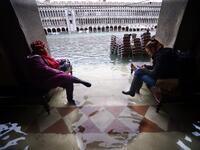 People sit on benches in a flooded arcade by St. Mark's Square on November 15, 2019 in Venice, two days after the city suffered its highest tide in 50 years. Flood-hit Venice was bracing for another exceptional high tide on November 15, as Italy declared a state of emergency for the UNESCO city where perilous deluges have caused millions of euros worth of damage. Filippo MONTEFORTE / AFP