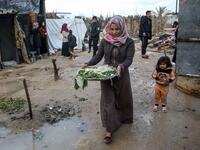 A Palestinian woman carries vegetables to her shack in Khan Yunis in the southern Gaza Strip on January 10, 2020. A family of 17, whose house was destroyed by an Israeli air strike last November, now live in a shack in cold weather and heavy rain. SAID KHATIB / AFP