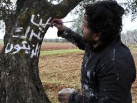 A Syrian man writes in white paint on the trunk of a tree the Arabic slogan "we will not abandon the olives", near the frontline between Syrian government forces and Turkish-backed opposition fighters in the town of Sarmin in the northern Syrian Idlib province on February 4, 2020. Omar HAJ KADOUR / AFP