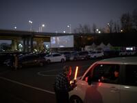 In a photo taken on March 21, 2020 an usher directs customers and their cars to a movie screen at a drive-through cinema in Seoul. Box office numbers in South Korea -- which has 8,897 confirmed virus cases -- have plummeted in recent weeks due to the epidemic, with authorities urging the public to avoid large crowds. But at drive-in cinemas, moviegoers can enjoy a movie from the comfort of their cars, parked in front of a large outdoor screen.  Ed JONES / AFP