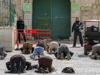 This picture taken on March 23, 2020 shows Palestinian Muslim men prostrate in prayer as Israeli security forces watch near the closed gate of the Aqsa mosque compound, which was closed by the Jordan Waqf religious authority administering the site as part of preventive measures against the spread of the COVID-19 novel coronavirus, in Jerusalem. Over a 24-hour period, in a world where a third of humanity is now under orders to stay home, AFP photographers have captured snapshots of daily life during the coro