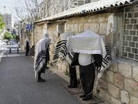 Ultra-Orthodox Jews, wearing the traditional Tallit Jewish prayer shawls, pray along a street outside their closed synagogue in Jerusalem on March 29, 2020, while keeping a distance of two metres from one another following instructions to stop the spread of the COVID-19 coronavirus pandemic. MENAHEM KAHANA / AFP