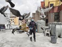 A pigeon owner, wearing personal protective equipment, watches his pigeons fly on the rooftop of his building in the southern suburb of Beirut on April 11, 2020. ANWAR AMRO / AFP