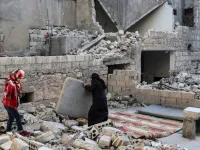 This picture taken on May 4, 2020 during the Muslim holy fasting month of Ramadan shows the mother of Tareq Abu Ziad (L), a displaced Syrian from the town of Ariha in the southern countryside of the Idlib province, preparing to put up a mattress so members of her family can sit to break their fast together for the sunset "iftar" meal, in the midst of the rubble of their destroyed home upon their return to the town for one day after fleeing during the previous military assault by Syrian government forces and
