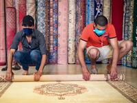 Moroccan rug dealers roll a carpet at a shop in the city of Sale, north of the capital Rabat, on June 3, 2020, during the novel coronavirus pandemic. Artisans in Morocco have been starved of income for almost three months because of the COVID-19 pandemic. The crafts industry represents some seven percent of GDP, with an export turnover last year of nearly 1 billion dirhams ($100 million). FADEL SENNA / AFP