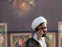 A Muslim cleric speaks on the phone in front of a poster depicting slain Iranian general Qasem Soleimani (L) and slain Iraqi commander Abu Mahdi al-Muhandis during a military parade for Hashed al-Shaabi (Popular Mobilisation) paramilitary force in the southern Iraqi city of Basra on June 14, 2020, marking the sixth anniversary of its founding after Iraq's top Shiite cleric Grand Ayatollah Ali Sistani called to defend the country from the Islamic State group (IS). Hussein FALEH / AFP