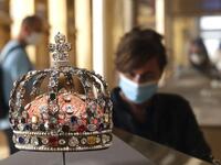 A visitor wearing face mask stands in front of the Crown of Louis XV held in the Apollo gallery at the Louvre Museum in Paris on July 6, 2020, on the museum' s reopening day. FRANCOIS GUILLOT / AFP