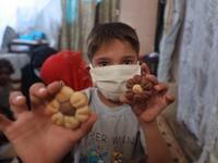 A displaced Syrian boy, wearing protective a face mask, displays cookies to the camera at a camp for the internally displaced near the town of Sarmada in Syria's northwestern Idlib province on July 29, 2020, as Muslims across the world are getting ready to celebrate Eid al-Adha. AAREF WATAD / AFP