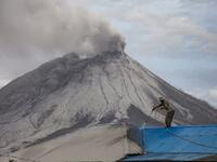 A villager cleans volcanic ash from his roof at Naman Teran village in Karo, North Sumatra, on August 11, 2020 a day after the eruption of Mount Sinabung (background). IVAN DAMANIK / AFP