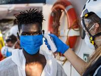 A crew member takes the temperature of a migrant  who has just been helped off Banksy's ship who is wearing protective clothes and a face mask (AFP)