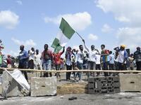 A protester raise the Nigerian national flag at a barricade mounted by potesters on the Lagos-Ibadan expressway to protest against police brutality and the killing of protesters by the military, at Magboro, Ogun State, on October 21, 2020. Buildings in Nigeria's main city of Lagos were torched on October 21, 2020 and sporadic clashes erupted after the shooting of peaceful protesters in which Amnesty International said security forces had killed several people. Witnesses said gunmen opened fire on a crowd of