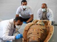 Archaeologists inspect a mummy, wrapped in a burial shroud adorned with brightly coloured hieroglyphic pictorials, during the unveiling of an ancient treasure trove of more than a 100 intact sarcophagi, at the Saqqara necropolis 30 kms south of the Egyptian capital Cairo, on November 14, 2020. Egypt announced the discovery of an ancient treasure trove of more than a 100 intact sarcophagi, the largest such find this year. The sealed wooden coffins, unveiled on site amid fanfare, belonged to top officials of 