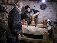Syrian-Armenian potter Misak Antranik Petros watches his son Anto moulding a clay vase at his workshop located inside an ancient mud-brick house near the city of Qamishli in Syria's northeastern Hasakeh province, on December 19, 2020. Petros was only a teenager when he had to take over for his sick father and become the main potter of the family. He has since become a master of the craft, and is keen to pass his skills on.  Delil SOULEIMAN / AFP