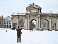People take pictures in front of the Puerta de Alcala in Madrid on January 10, 2021. Snowstorms in Spain left three people dead and caused chaos across much of the country, trapping motorists and shutting down the capital's air and rail links. Gabriel BOUYS / AFP