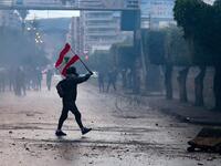A Lebanese anti-government protester waves a national flag during clashes with security forces in front of the Serail (headquarters of the Governorate), in the northern port city of Tripoli, following a demonstration to protest against the economic situation, on January 28, 2021. Tripoli was already one of Lebanon's poorest areas before the coronavirus pandemic piled new misery onto a chronic economic crisis. Many of its residents have been left without an income since Lebanon imposed a full lockdown earlie