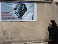 An Iraqi woman walks in front of a banner welcoming Pope Francis