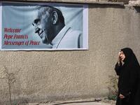 An Iraqi woman walks in front of a banner welcoming Pope Francis