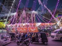 Vehicles, motorcycles, and tuk-tuks (motorised rickshaws) drive past a stall selling Ramadan lanterns 