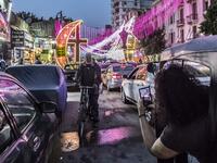 A woman riding in a tuk-tuk (motorised rickshaw) peeks out to use her phone to photograph a man riding a bicycle