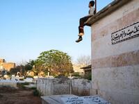 A boy sits atop a grave with a sign quoting the Holy Koran 