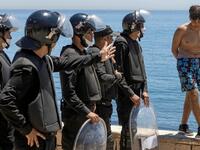 Moroccan police speak to a migrant as he stands on a sea wall in the northern town of Fnideq after attempting to cross the border from Morocco to Spain's North African enclave of Ceuta on May 19, 2021. Spain stepped up diplomatic pressure on Rabat as its prime minister flew into Ceuta, vowing to "restore order" in the North African enclave after a record 8,000 migrants reached its beaches from Morocco.