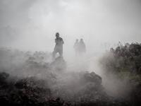 Men cross the front of the still smoking lava rocks from an eruption of the Mount Nyiragongo on May 23, 2021 in Goma in the East of the Democratic Republic of Congo. A river of boiling lava came to a halt on the outskirts of Goma Sunday, sparing the city in eastern DR Congo from disaster after the nighttime eruption of Mount Nyiragongo sent thousands of terrified residents fleeing in panic. Fire and strong fumes emanated from the blackish molten rock as it swallowed up houses
