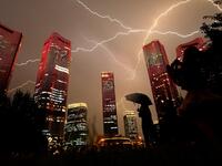 A bolt of lightning crosses the sky as people look at buildings displaying a light show on the eve of the 100th anniversary of the Chinese Communist Party in Beijing 