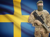 جندي يحمل بندقية رشاشة وخلفه العلم الوطني - السويد