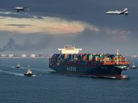 صورة خارجية لسفينة حاويات كبيرة تعبر مضيق هرمز، مع أجواء توحي بالتوتر في المشهد. السفينة محمّلة بالكامل وترفع علمًا محايدًا،