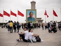 A couple sit back-to-back past a portrait of nationalist leader Sun Yat-sen in Tiananmen Square on the May Day holiday in Beijing on May 1, 2018 / AFP