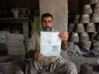 In this photo taken on October 10, 2018.Afghan potter Shirin Agha, 45, poses for a picture as he holds his id card or Tazkira registered to vote in the upcoming parliamentary election at his workshop, on the outskirts of Jalalabad. 
NOORULLAH SHIRZADA / AFP