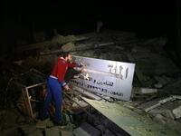 Palestinian men point at an insurance company sign amid the rubble of a building that collapsed from reported Israeli strikes in Gaza City on March 25, 2019. 
MOHAMMED ABED / AFP