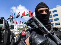 A member of the Rapid Intervention National Brigade (BNIR) of the Tunisian security forces standing guard by the national flags of the Arab League member states, outside Council of Arab Interior Ministers' headquarters, ahead of the Arab League summit due to take place in Tunis. 
FETHI BELAID / AFP