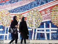 To women walks along a street past a mosaic mural on the first anniversary of the nuclear agreement in Tehran (Twitter)