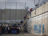 Palestinians climb over the barrier wall
