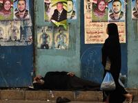 An Egyptian woman walks past a man sleeping next to a wall decorated with election campaign posters next to a polling station in Cairo, as the nation of some 41 million eligible voters goes to the polls.