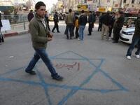 A Palestinian youth walks on a Star of David sprayed on the ground with Al-Jazeera written in red Arabic letters in the middle during a demonstration in the West Bank city of Ramallah.