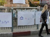 A Palestinian woman walks past placards denouncing Al-Jazeera during a protest near the offices of the pan-Arab news channel.