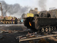 An army tank stands near the remains of a burnt out armored personnel carrier in Tahrir Square.