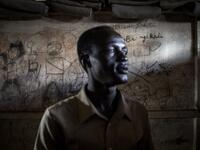 John Aremic, 20, a South Sudanese Refugee stands in front of a wall filled with drawings and writings depicting scenes from home in a building located in a transition camp for South Sudanese refugees who have just arrived in Aru. JOHN WESSELS / AFP
