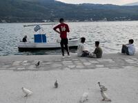 Migrant youth sit by a local fisherman at the city of Vathy on the island of Samos.  LOUISA GOULIAMAKI / AFP