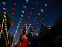 A couple walks past "casetas" (stalls) during the "Feria de Abril" (April Fair) festival in Seville on May 6, 2019. The fair dates back to 1847 when it was originally organized as a livestock fair but has turned into a week of flamenco dancing, music and bullfighting.  CRISTINA QUICLER / AFP
