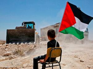 A Palestinian boy sits on a chair with a national flag as Israeli authorities demolish a school site in the village of Yatta, south of the West Bank city of Hebron and to be relocated in another area, on July 11 2018. (Hazem Bader/AFP / Getty Images)