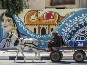 Palestinians ride a donkey cart past a mural along a street in Rafah, in the southern Gaza Strip, on September 25, 2019. SAID KHATIB / AFP